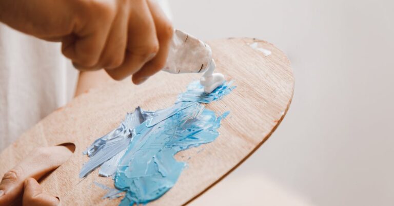 Close-up view of a hand mixing blue paint on a wooden palette, emphasizing texture and creativity.