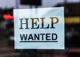 Close-up of a Help Wanted sign taped to a glass window in a storefront.
